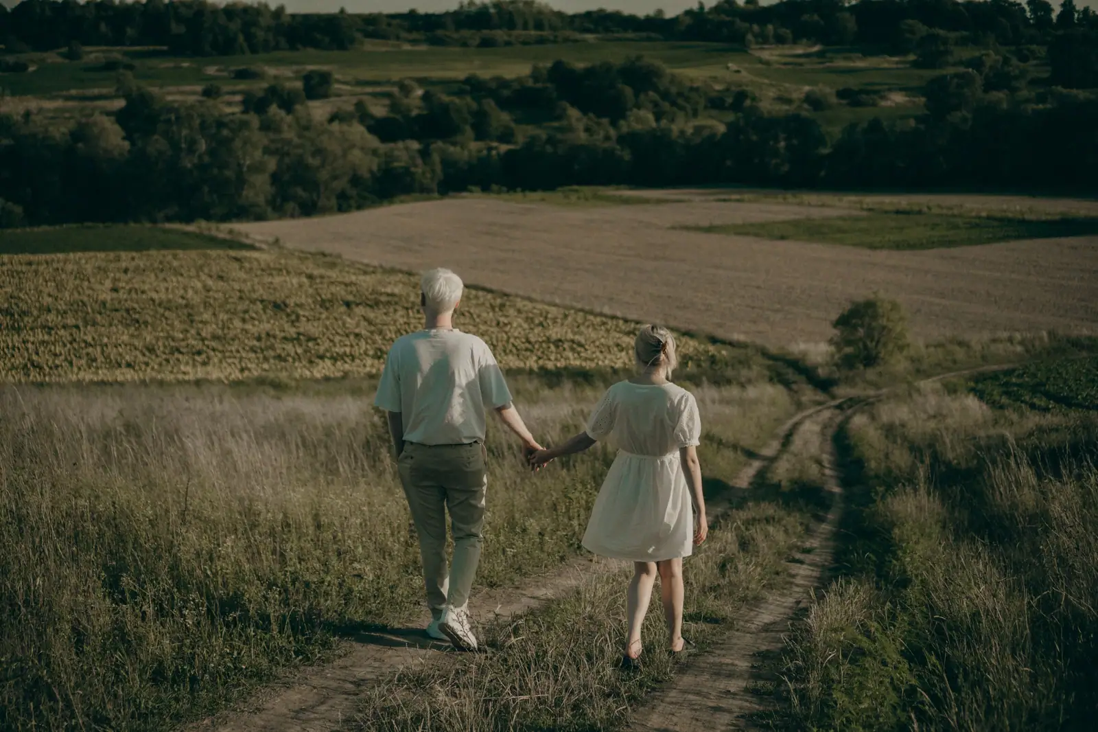 An older couple walking side by side along a country lane through green fields