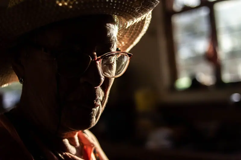A patient in a straw hat resting by a sunny window at home