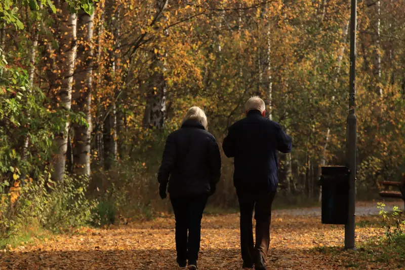 An older couple walking a wooded path in autumn
