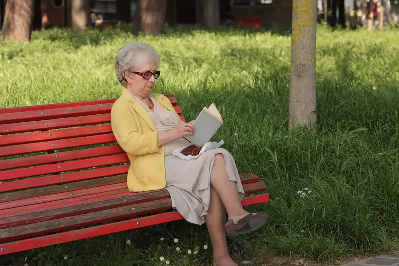 A grandmother reading on a red park bench in the sun