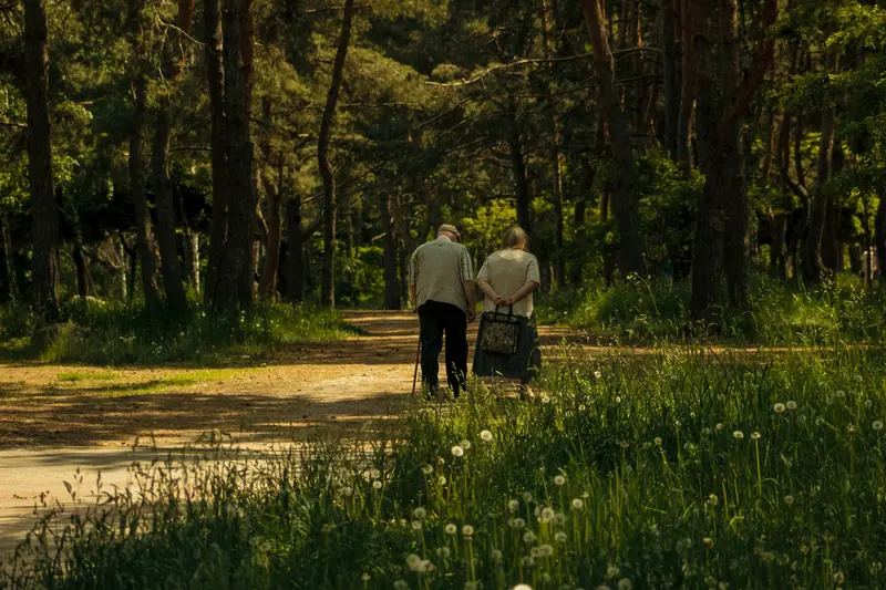 A couple walking slowly down a shaded path through tall grass
