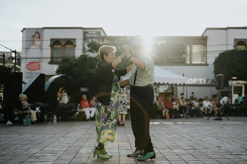 An older couple dancing in a sunny plaza