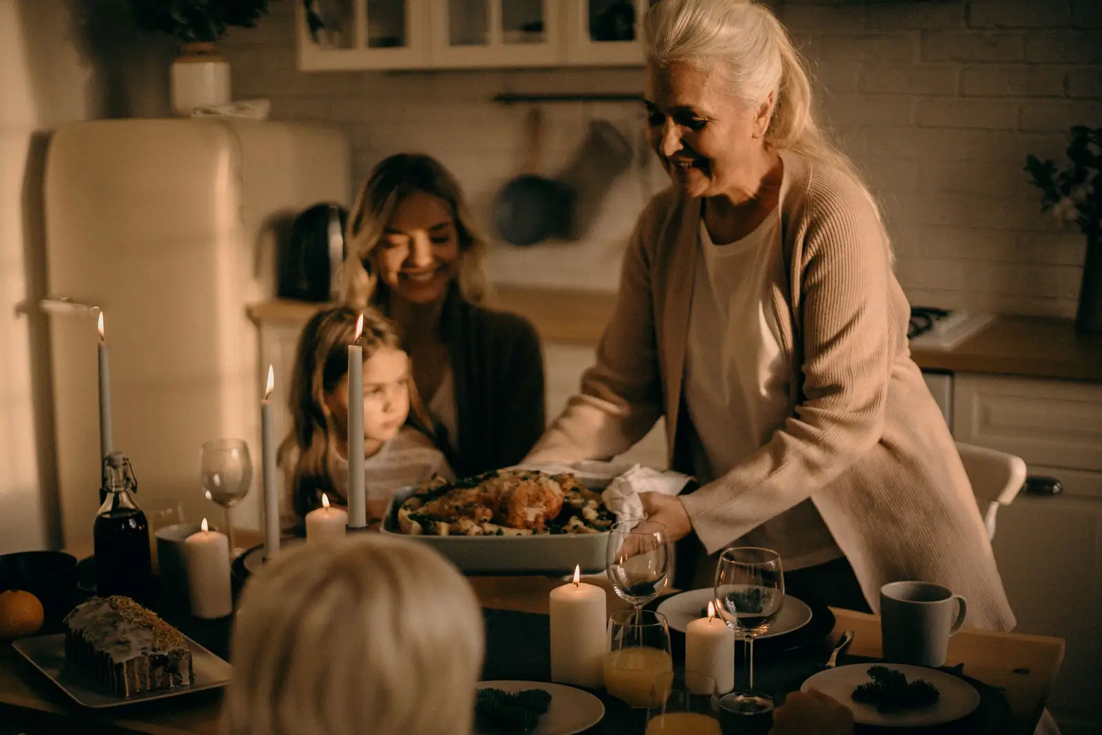 A grandmother setting a roast on the candlelit kitchen table for her family