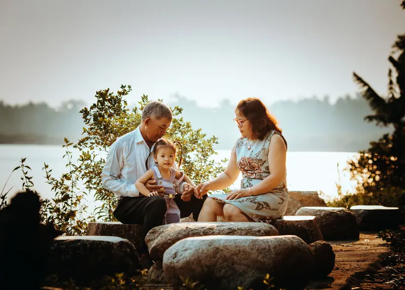 A grandfather holding his grandbaby beside the water while the family visits
