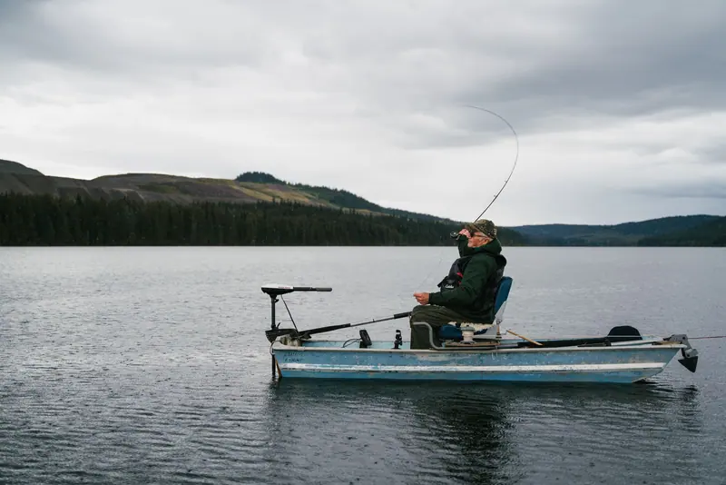 A man fishing from a small boat on a still lake
