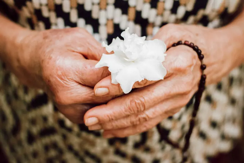 Old hands holding a white flower and prayer beads