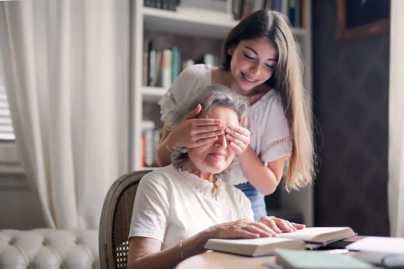 A granddaughter covering her grandmother's eyes as a surprise