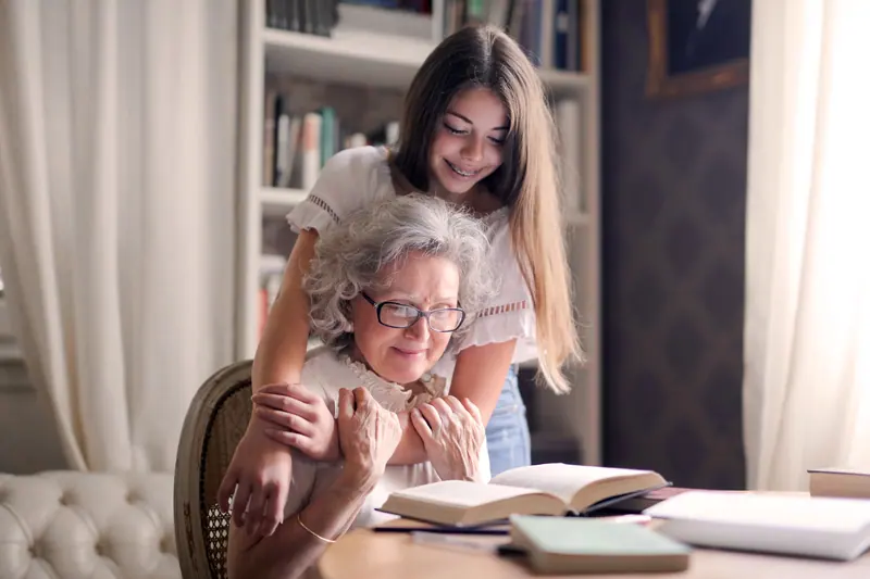 A granddaughter wrapping her arms around her grandmother at the table