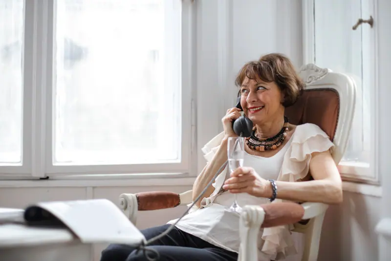 A woman chatting on her old telephone with a glass of champagne