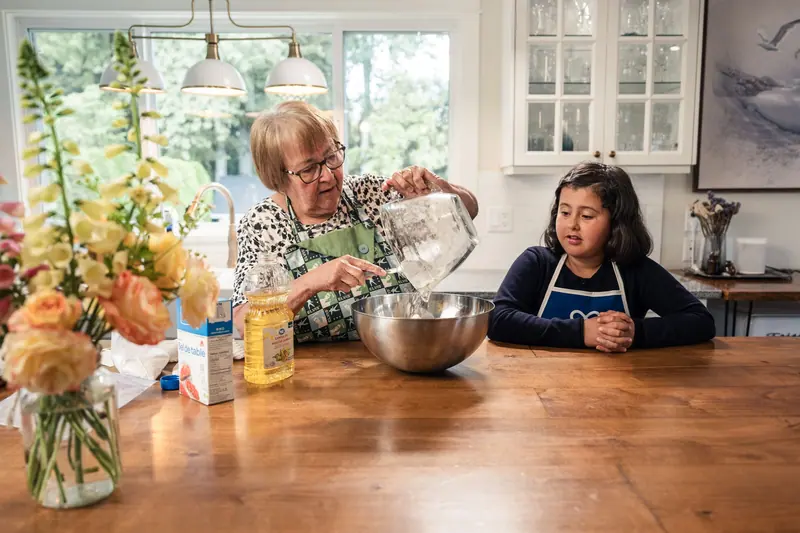 A grandmother mixing a cake batter with her granddaughter at the kitchen table