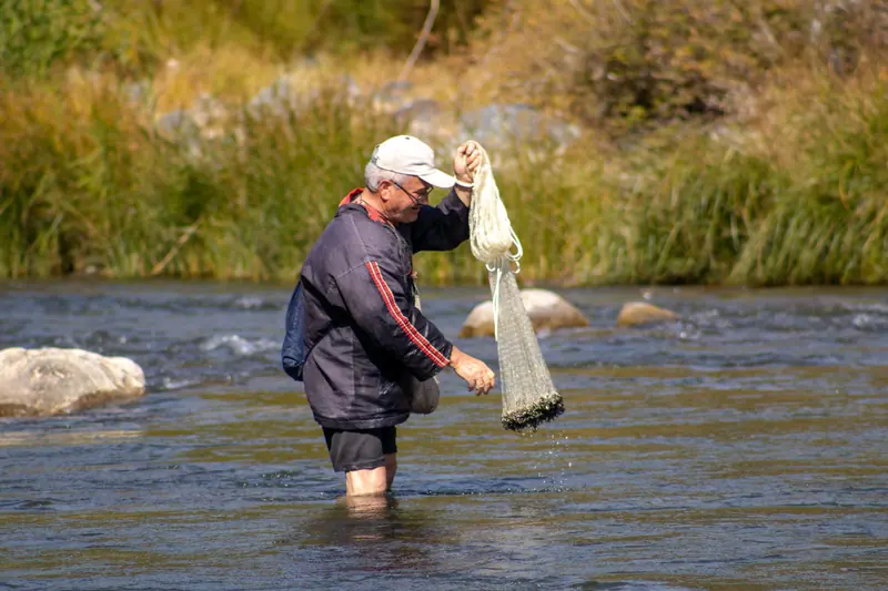 A man wading into the shallows with his cast net