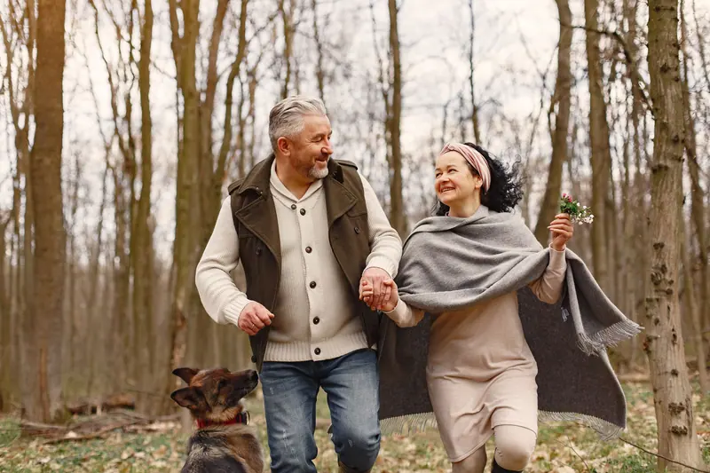 An older couple laughing on a walk in the woods with their dog