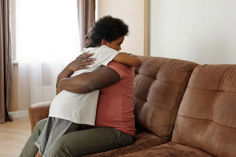 A daughter hugging her mother on the living room couch