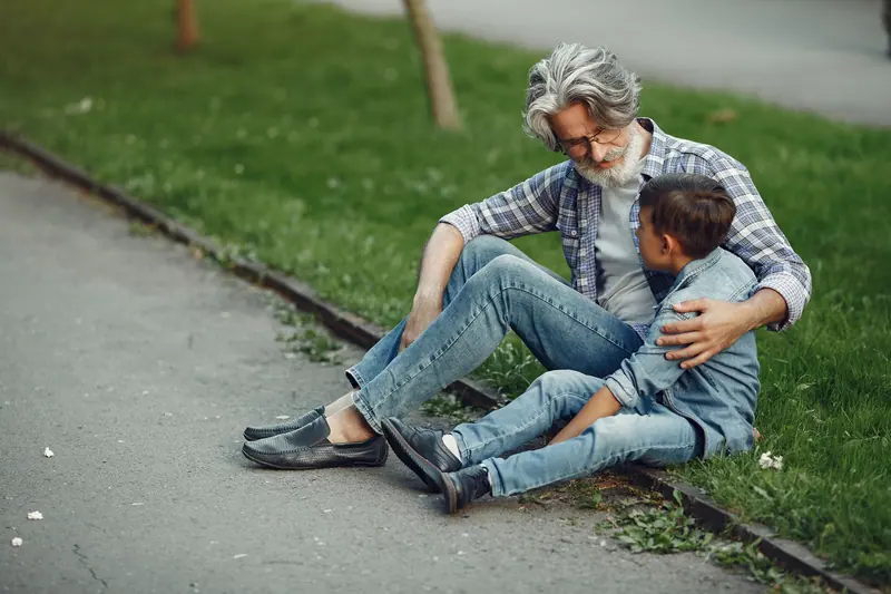 A grandfather hugging his grandson on the grass by the path