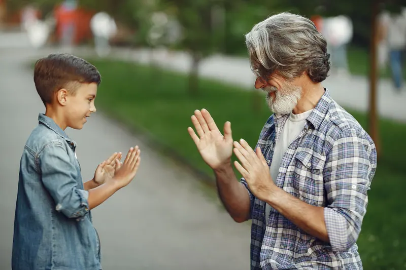 A grandfather and grandson playing a clapping game outdoors