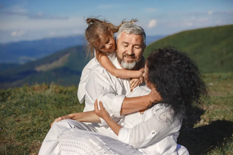 Grandparents hugging their granddaughter on a hilltop