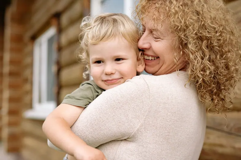 A grandmother hugging her grandson against a log wall