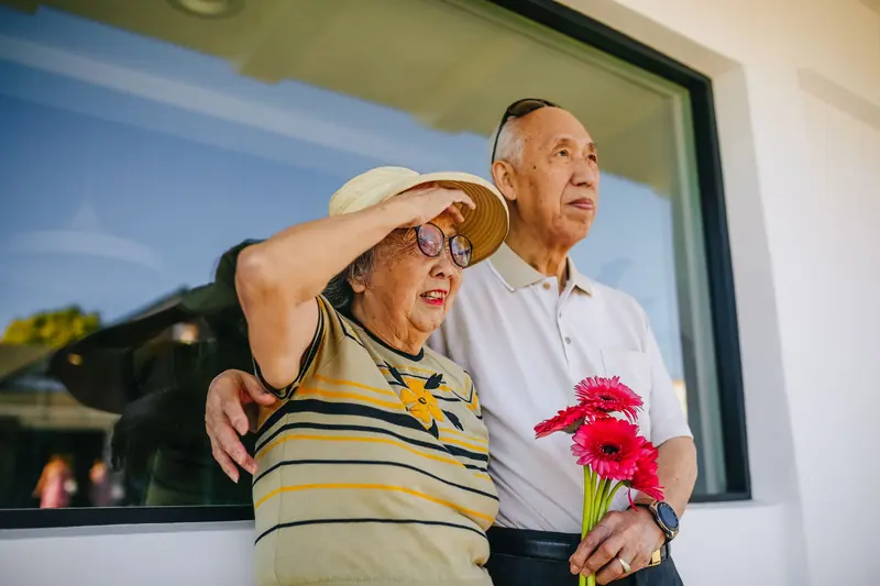 A married couple laughing together with a bouquet of red flowers