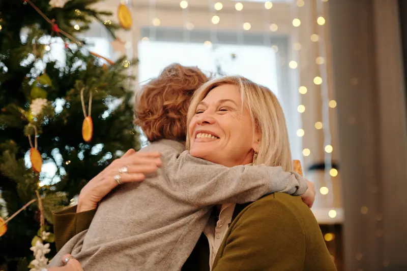 A daughter hugging her mother by the Christmas tree