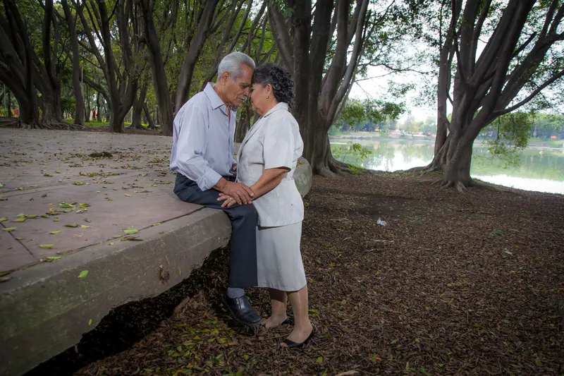 An old couple leaning their foreheads together by the lake