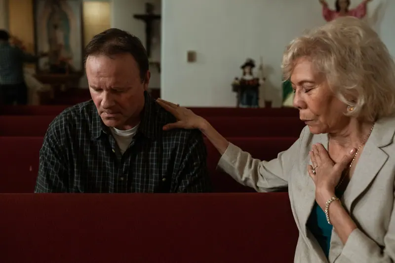 A chaplain praying with a son in a quiet church pew