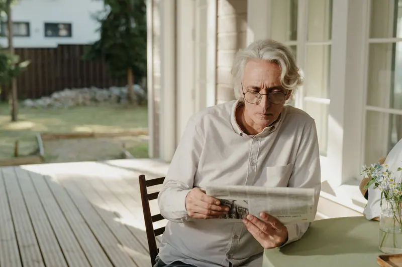 A patient reading the paper at the table by the open porch door