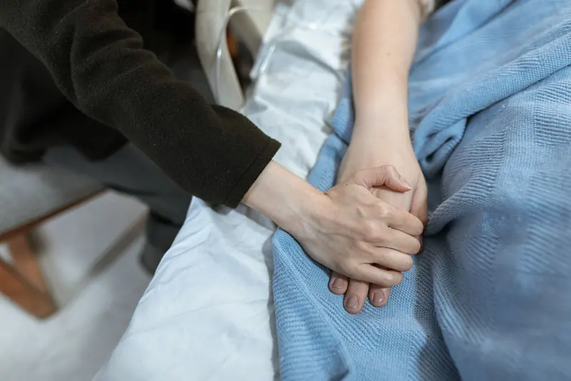 A nurse's hand holding a patient's under the blanket