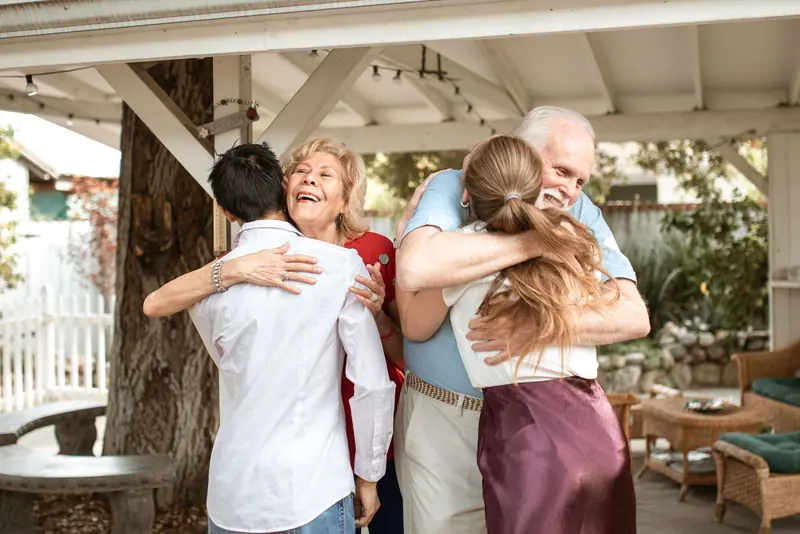 A family hugging hello under the backyard pergola