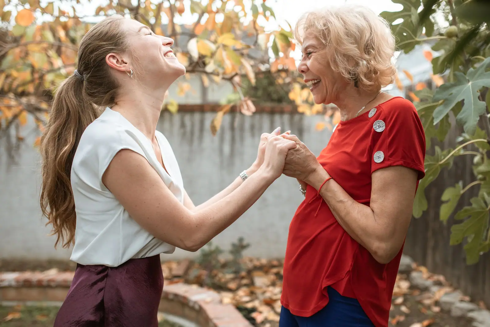 A grown daughter and her mother holding hands and laughing together in the garden