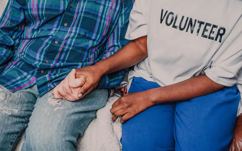 A volunteer sitting close and holding a patient's hand
