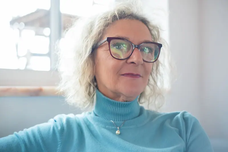 A woman in a blue turtleneck smiling by the window