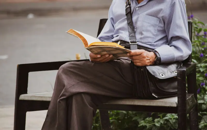 A patient reading a paperback on a bench outside