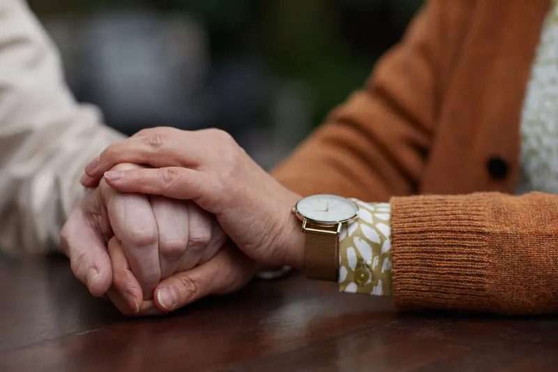 A daughter's hand folded over her mother's on the kitchen table