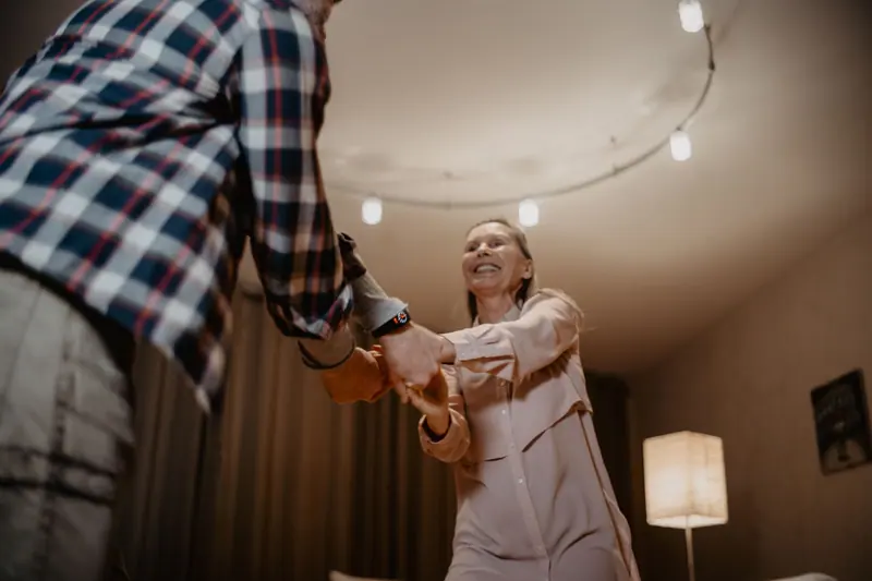 An older couple laughing as they dance at home