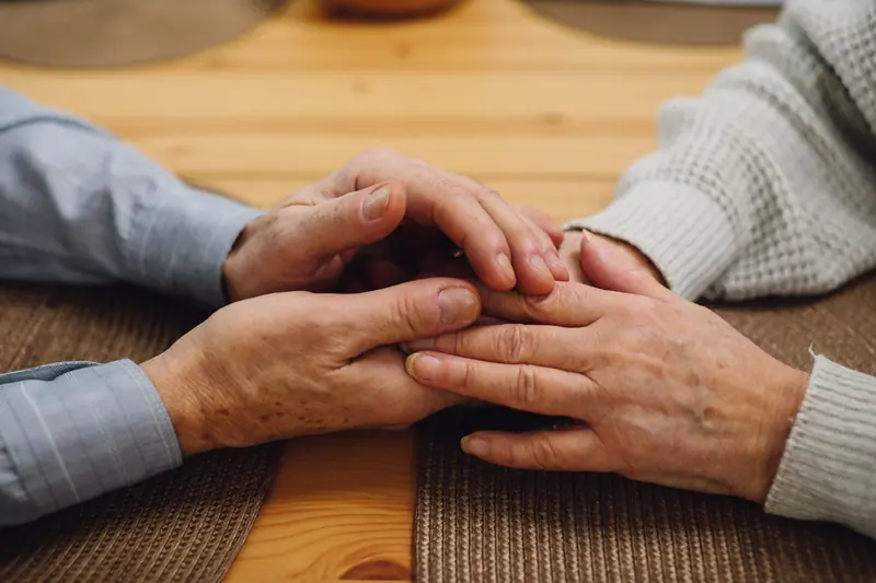 An old married couple's hands folded together on the table