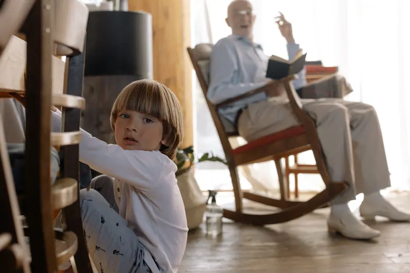 A grandfather in his rocking chair while his grandson plays nearby