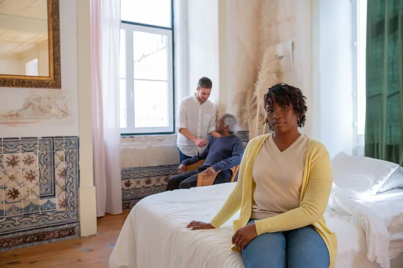 A caregiver sitting with a patient in his bright bedroom