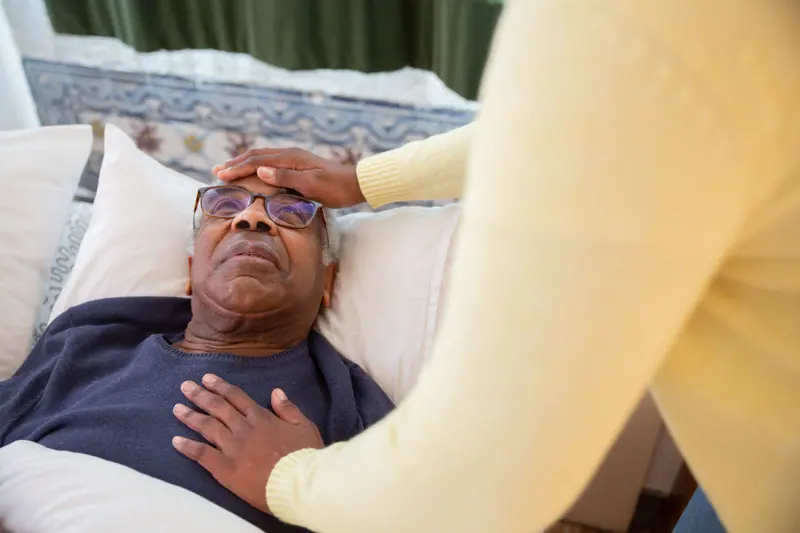 A caregiver resting her hand on a patient's forehead