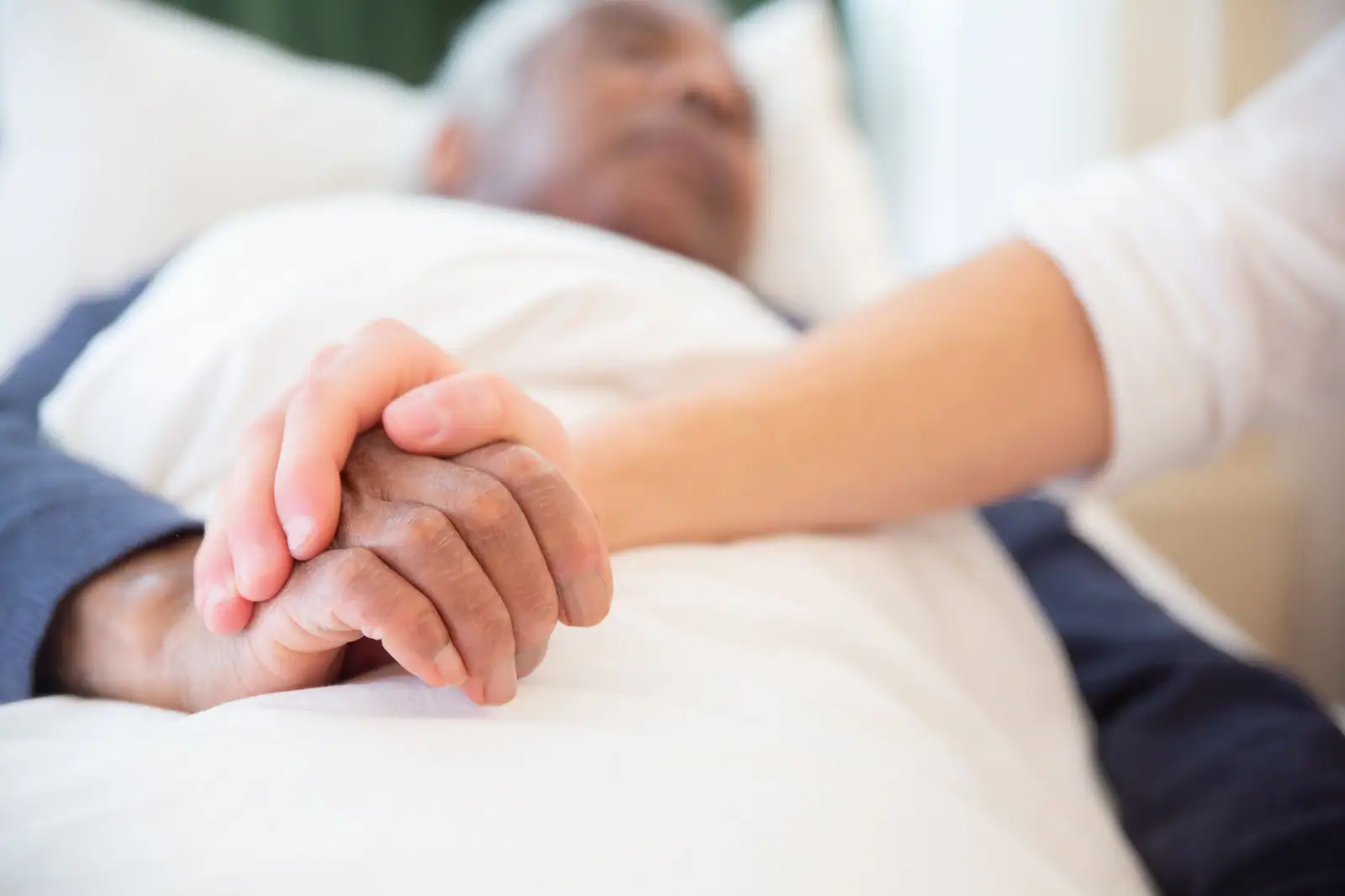 A nurse holding a patient's hand as he rests