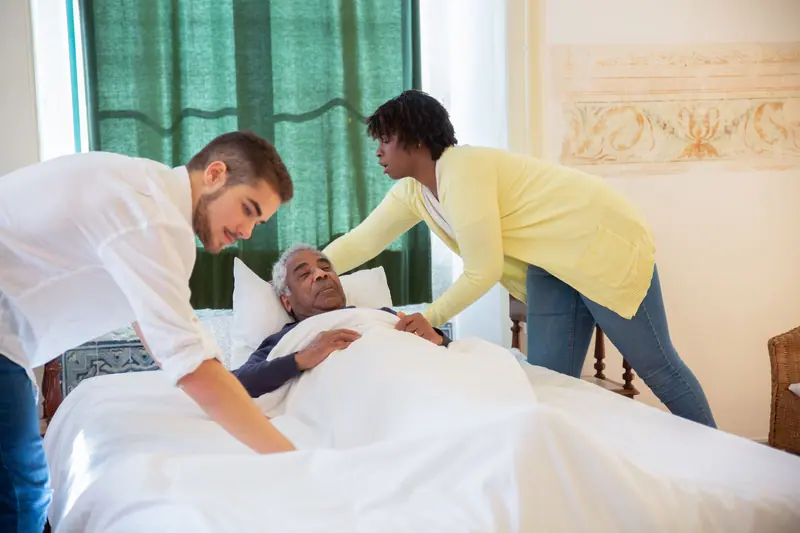 Two caregivers helping a patient get comfortable in bed