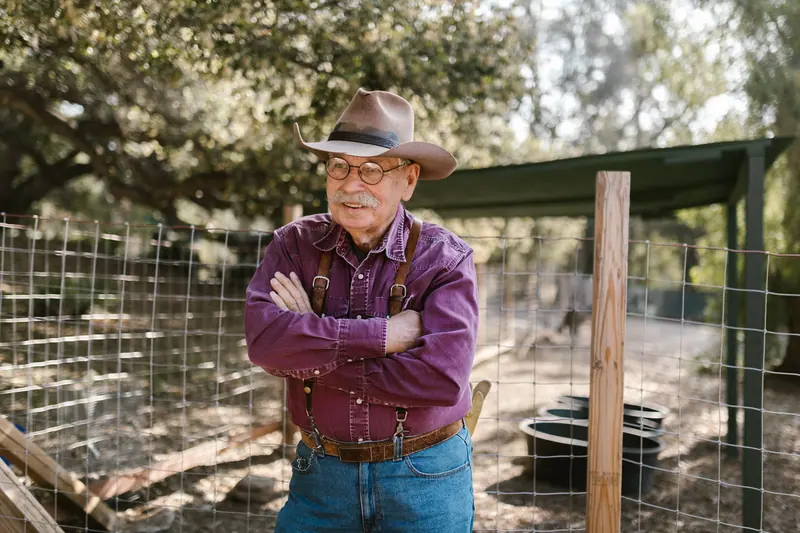 The same rancher standing by his pens with his arms crossed and a half smile