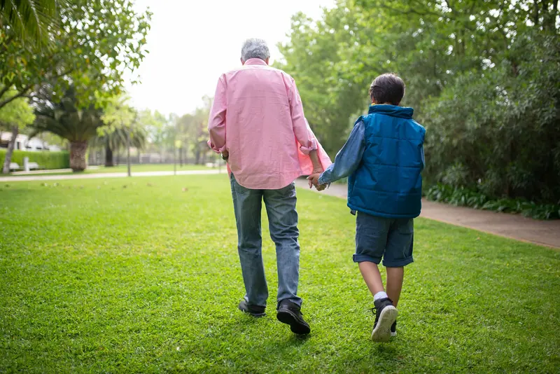 A grandfather and grandson walking hand in hand across the lawn