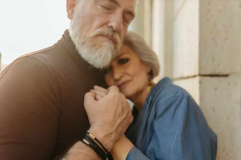 An older couple holding each other close by the window