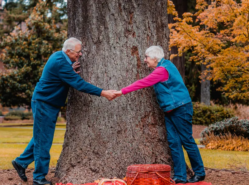 An older couple holding hands beside a tree in autumn