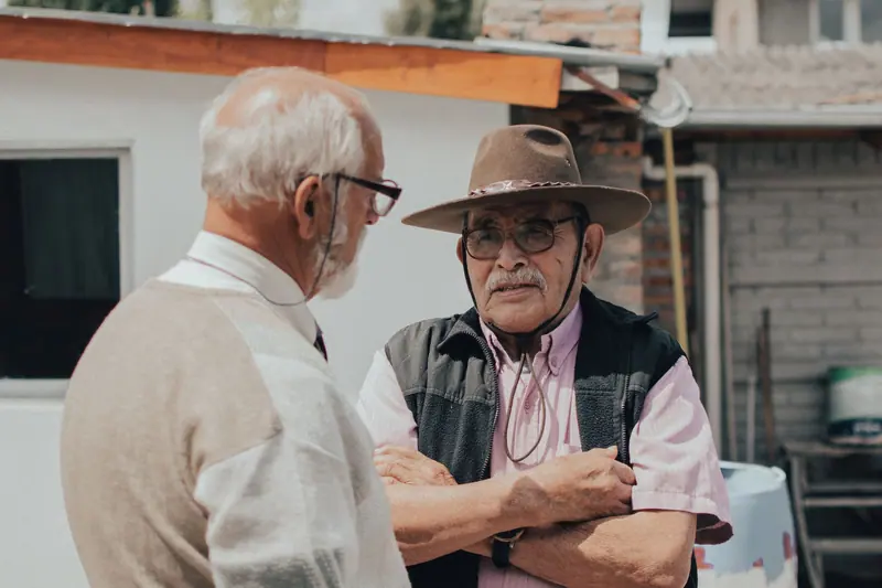 A chaplain talking with a patient in a cowboy hat outside his house