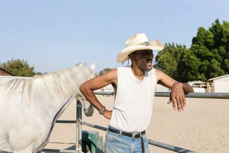 A rancher leaning on the fence beside his white horse