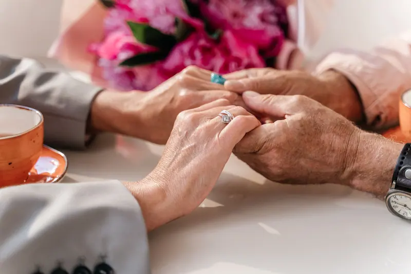An old married couple holding hands over coffee and a bunch of roses