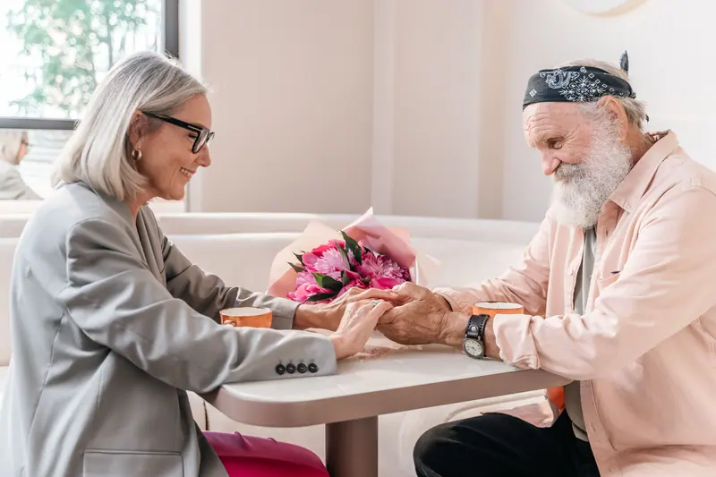 An older couple holding hands across a café table with flowers