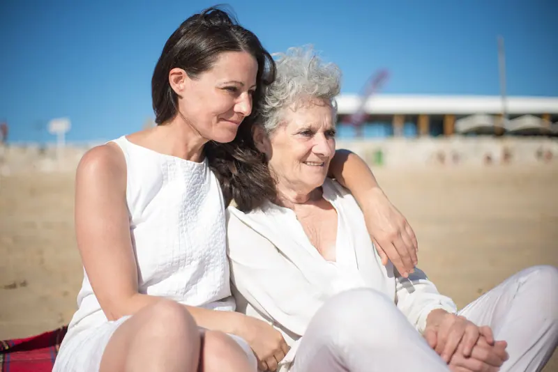 A mother and daughter sitting close on the sand