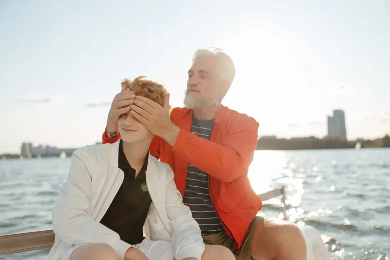 A grandfather playfully covering his grandson's eyes on the boat